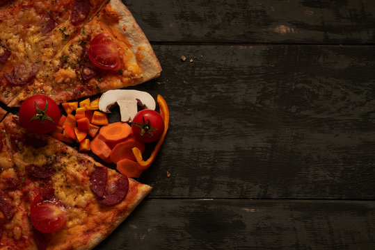 half pizza and vegetables on wooden table background