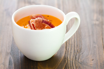 cold soup with smoked meat in white cup on brown wooden background