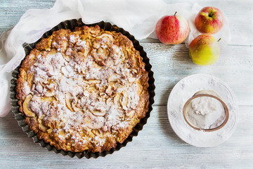Homemade sweet fruit cake in baking dish on wooden background. Made with apples, almond, vanilla and icing sugar. Top view