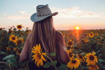 Fototapeta na wymiar Girl in a cowboy hat in a sunflower field. Sunset