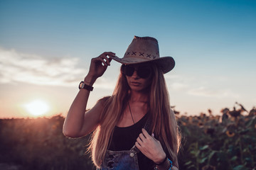 Girl in a cowboy hat in a sunflower field. Sunset