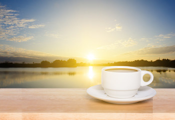 white coffee cup on wood table and view of sunset in the river background