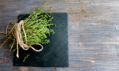 Heap of thyme twigs on black plate. Wooden table. Top view, Closeup. Copy space. 