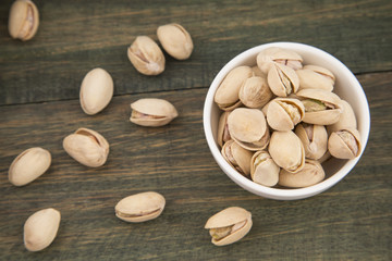 White bowl of pistachios on wooden background