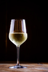 Chilled dry white wine in the glass, vintage wooden background,
