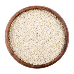 Sesame seeds in a wooden bowl on white background. Dried seeds with removed seed coats. Sesamum, also called benne. Edible, raw, organic and vegan food. Isolated macro photo close up from above.