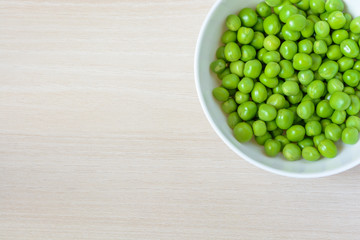 Fresh green peas in white ceramic bowl on wooden background. Top view.