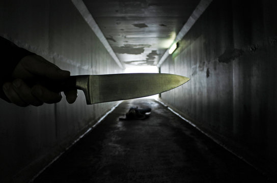 Man hand holds a knife over a murder victim in a dark tunnel