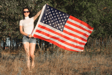 The girl with the American flag outdoors, stars and stripes flag flutters in the wind,