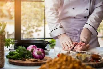 Man with knife cuts meat. Chef stands near frying pan. Pork meat for frying. Professional cook in the kitchen.