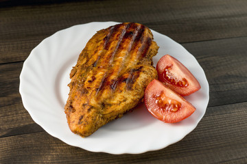 grilled chicken breast with tomatoes served on white plate on wooden table