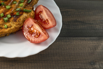 grilled chicken breast with tomatoes and chive served on white plate on wooden table
