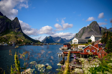 Reine in Lofoten Islands, Norway, with traditional red rorbu huts under blue sky with clouds. 