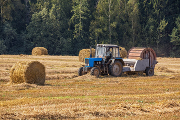 Obraz premium Agricultural machines working in the field. Special machine to collectthe straw. The tractor-trailer running on the field. Harvest