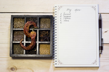 Set of spices in dark wooden case near the notebook and pen to list ingredients
