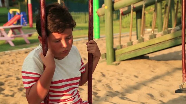Lonely, sad preteen boy sitting on the swing at the playground