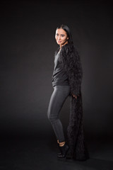 Beautiful brunette lady posing in full length over dark background. Lady with long black hair looking at camera.