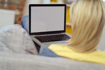 frau sitzt auf der couch und schaut auf ihren laptop