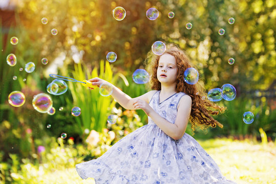 Cute curly girl in flying dress playing with soap Bubbles. Happy