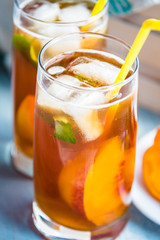 Glasses with homemade ice tea, peach flavored. Freshly cut peach slices for arrangement. Light blue wood background.