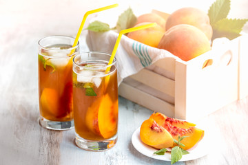 Glasses with homemade ice tea, peach flavored. Freshly cut peach slices for arrangement. White crate full with peaches in the background.