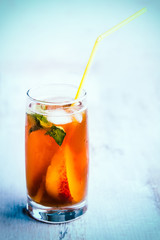 A glass with homemade ice tea, peach flavored. Freshly cut peach slices for arrangement. Light blue wood background. background.