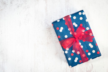 Obraz premium Gift box wrapped in blue dotted paper with red ribbon on a white wood old background