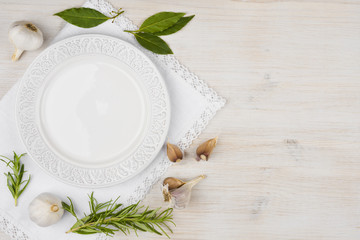 White plate with garlic, bay leaf and rosemary on wood