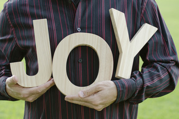 Wooden letters of the word joy - close up of man's hands holding the word with a Holiday themed red plastic container.