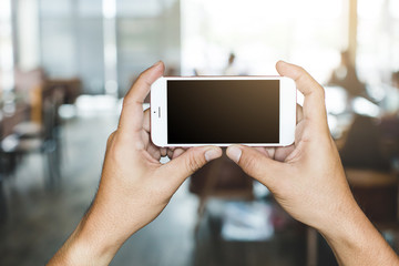 hand holding white  smartphone with blank screen in coffee shop