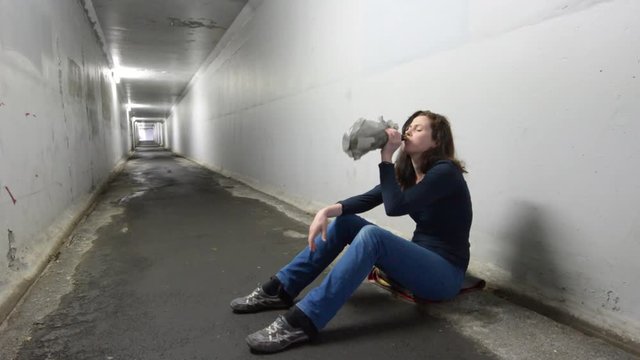 Drunk woman drinks alcohol in a tunnel. Women alcoholism concept. Real people, copy space