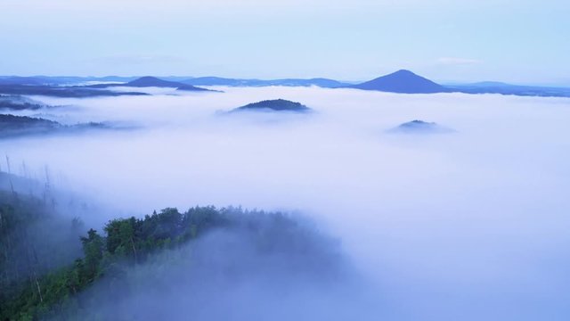 Time lapse. Hilly landscape after rainy night. Foggy valley bellow view point full of creamy mist. The fog is moving over treetops of forest. First pink sunrays of daybreak colored sky.