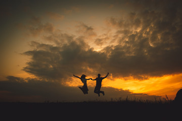 Young couple hold their hands tightly while jumpung under golden