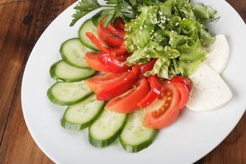 vegetable mix (salad, cucumber, tomato, parsley) and cheese on a white plate. wooden background.