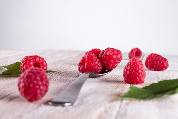 Closeup of ripe and fresh raspberries in metallic spoon and sprinkled on wooden desk