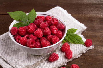 View from above on handful of ripe and fresh raspberry in white cup and some raspberry sprinkled on white wooden desk