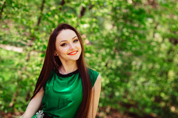 Fototapeta premium Green-eyed girl poses in green dress before green trees