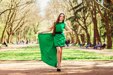 Delightful woman spreads her dark green dress while posing in th