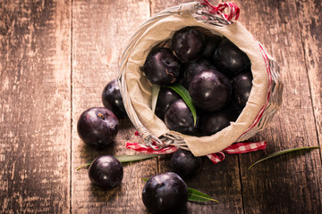 Fresh plums in a basket on rustic wooden table.