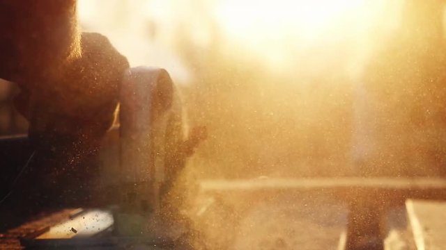 Man is craft working at a work bench with power tools in slowmotion during sunset with beautiful lens flare. 1920x1080