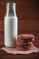 Pair of fresh baked cookies with chocolate with bottle of milk on wooden table