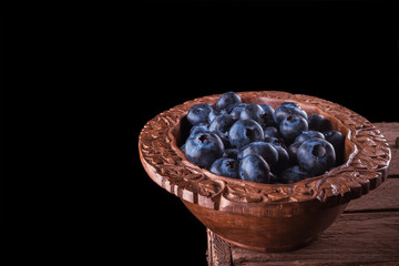 View from above on handful of ripe and fresh blueberries in brown wooden cup and some blueberries sprinkled on white wooden desk