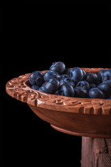 View from above on handful of ripe and fresh blueberries in brown wooden cup and some blueberries sprinkled on white wooden desk