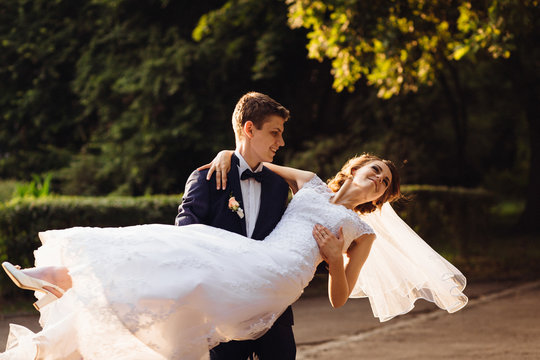Young groom whirls elegant bride in the park