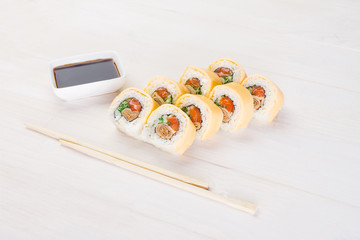 Sushi roll on wooden background . They were 8 pieces .Lay next to sticks and is dishes with sauce.