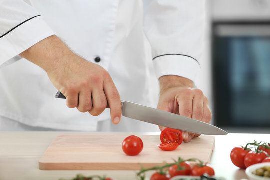 Chef cutting tomato on wooden board in kitchen