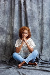 Fototapeta premium Young beautiful african girl sitting at floor over grey background.