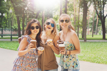 Three beautiful young boho chic stylish girls walking in park.