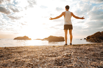 Man athlete standing with arms raised and looking at sunset