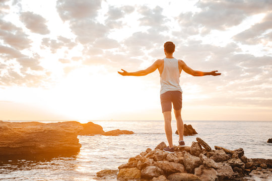 Athlete Standing Backwards With Arms Raised At The Rocky Beach